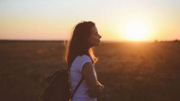 a happy woman standing in a field at sunset.