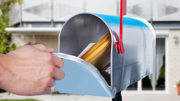 Opening door on metal mailbox with red flag raised yellow envelopes inside.