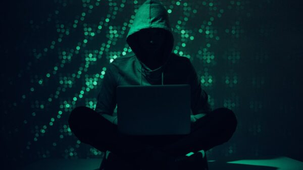 person in a hoodie in the dark with computer code behind them.
