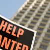 black sign with orange lettering saying help wanted in front of a building.