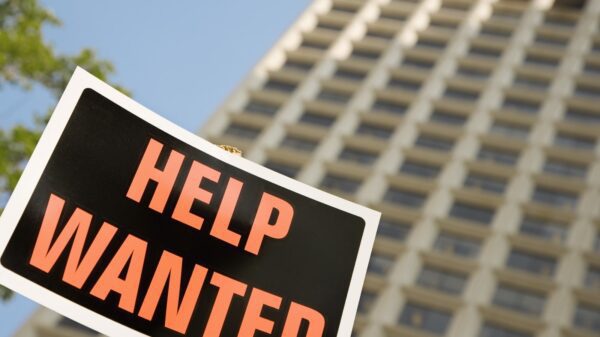 black sign with orange lettering saying help wanted in front of a building.