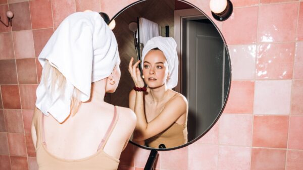 Woman washing her face in the mirror with a towel on her head.