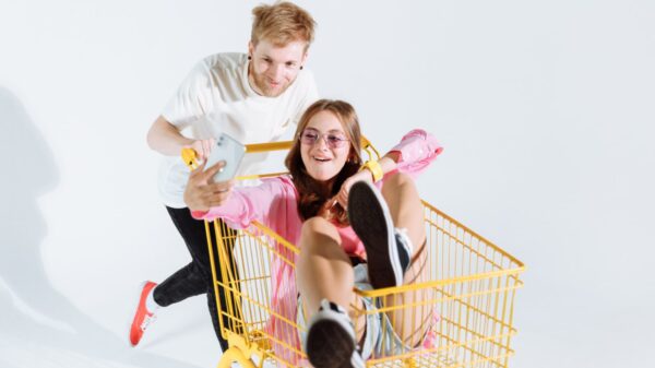 Guy pushing girl in a shopping cart while girl is recording it on her phone.