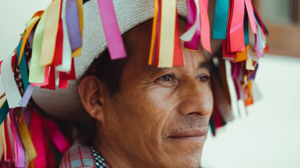 Close up picture of an indigenous man wearing a traditional hat.