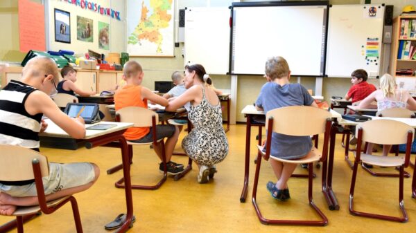 Teacher kneels at a student's desk in a full classroom.