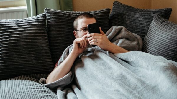 Man laying on couch with blanket on looking at his phone.