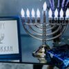 A happy Hanukkah image sits on a table with a lit menorah.
