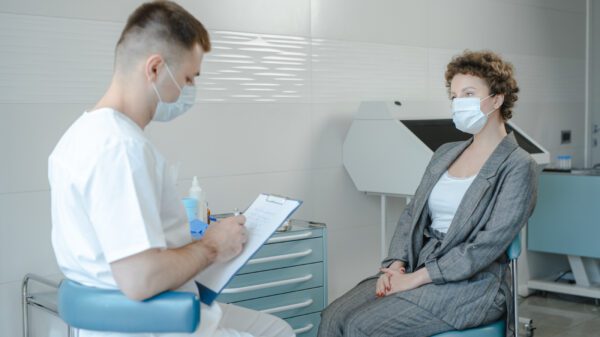 a doctor listening to a woman in business attire wearing masks.