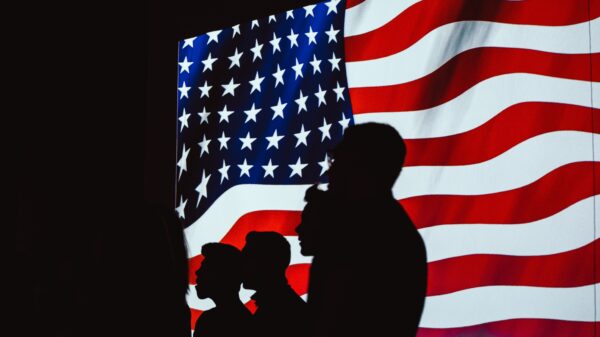 Silhouettes of people in front of a flag.
