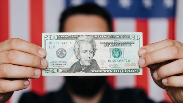 A blurred man holding a 20 dollar bill in front of a flag.