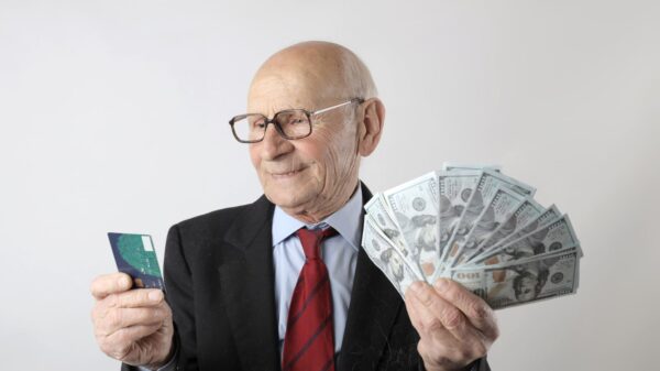 An old man in a suit holding cash and a credit card.