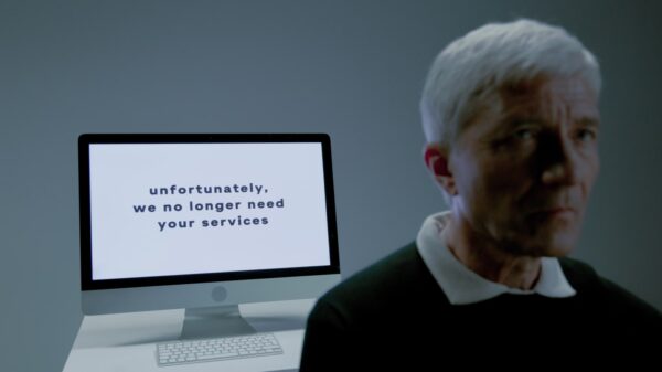 An elderly man facing away from a computer screen.